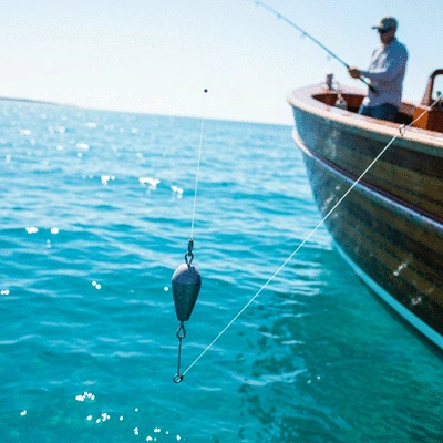 Close-up of a downrigger weight being lowered into clear blue water from a fishing boat